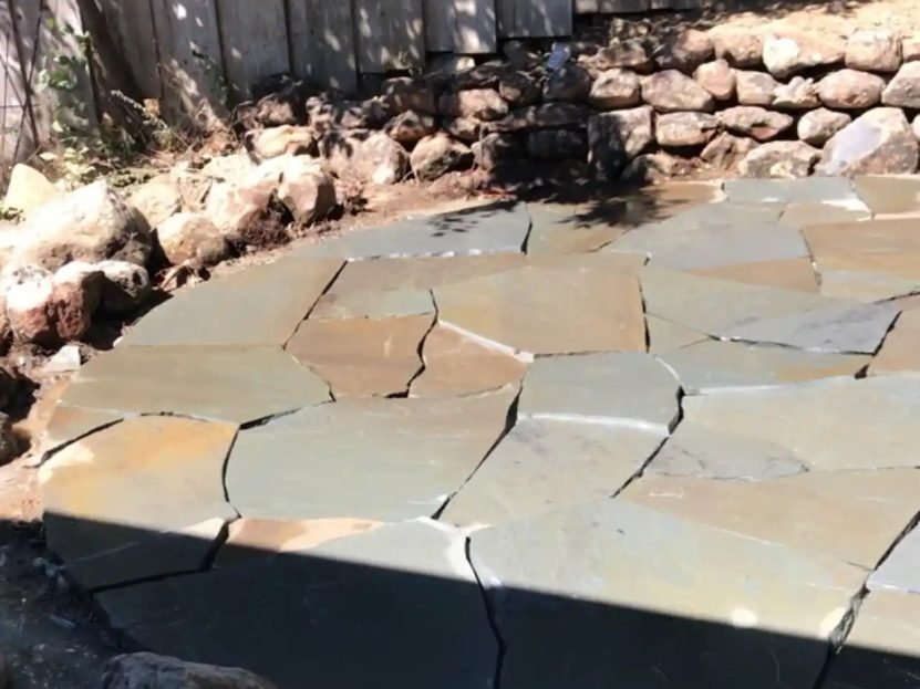 Flagstone patio installation close-up against a stone wall